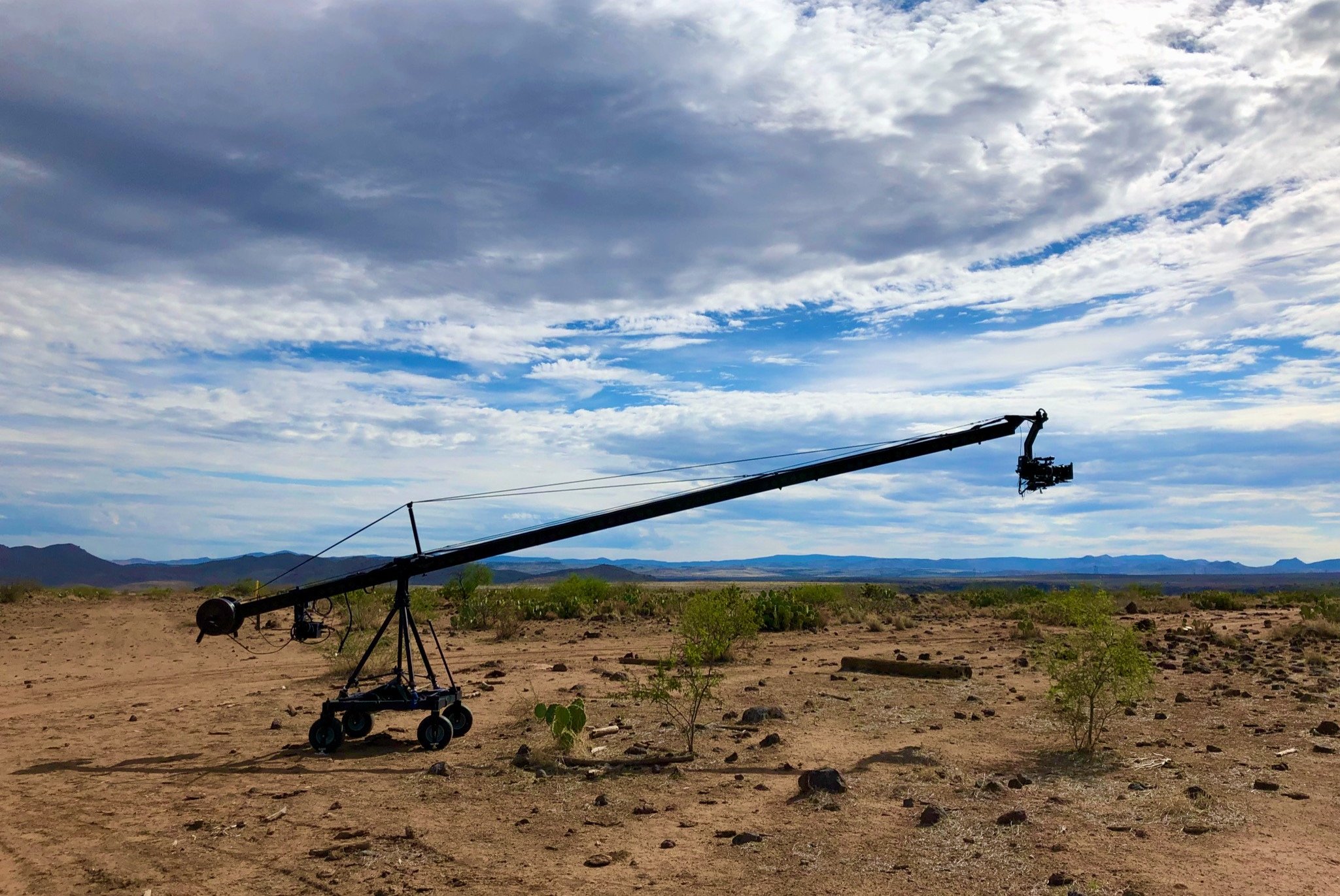 A camera Jib extending over rocky desert, the arm running diagonally to the camera head against a blue sky and clouds.