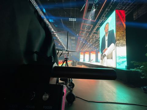 A camera rig and its monitor in near-darkness, facing a wall of screens.