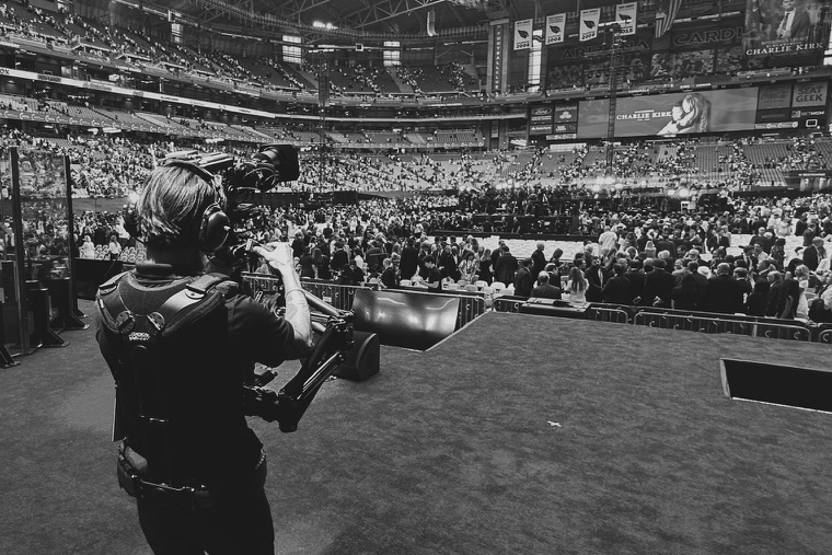 A Steadicam operator in a vest and harness with the camera on the rig's arm at head height, working the floor of a crowded arena during an event.