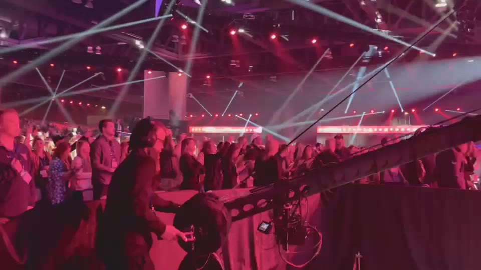 America Fest (2021) — Jib. Over a packed hall under magenta stage light, the Jib arm in the foreground and a lit banner across the far wall.
