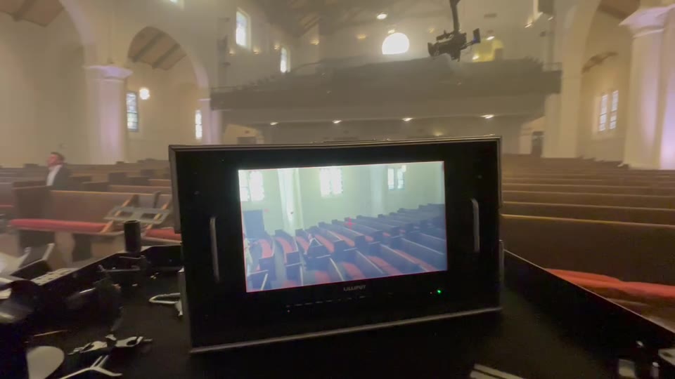 Jeff May Music Video (2021) — Jib. The set monitor carrying the live picture, the crane's camera head entering the top of the frame, the sanctuary's pews and arched windows beyond.